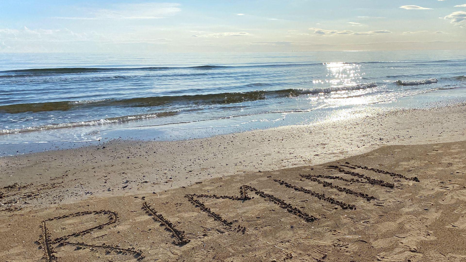 Spiaggia di Rimini con scritta sulla sabbia e mare calmo all'orizzonte.