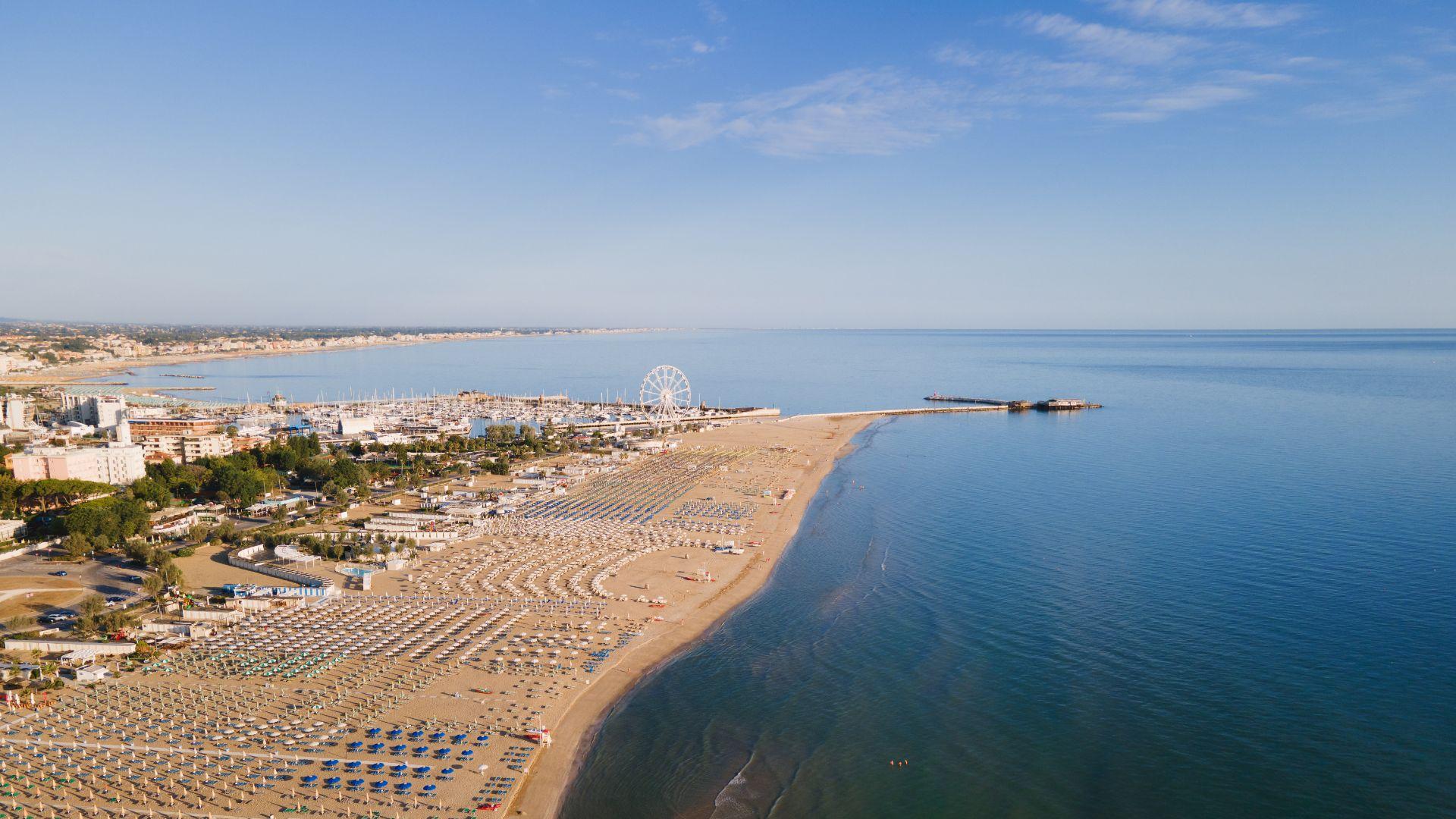 Spiaggia affollata con ombrelloni colorati e vista sulla ruota panoramica e il mare.