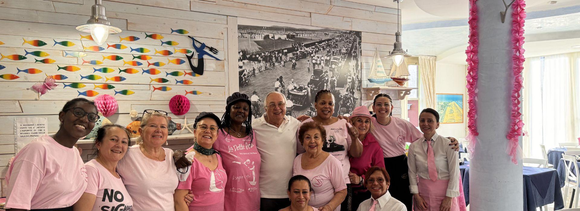 Gruppo di persone in un ristorante con magliette rosa, decorazioni vivaci e sorrisi.