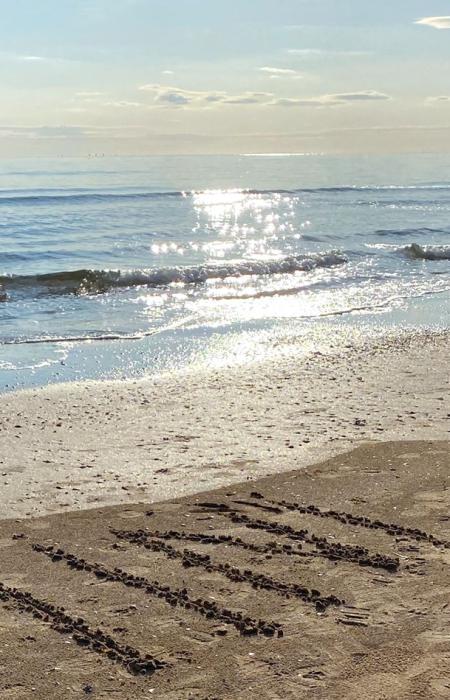 Spiaggia di Rimini con scritta sulla sabbia e mare calmo all'orizzonte.