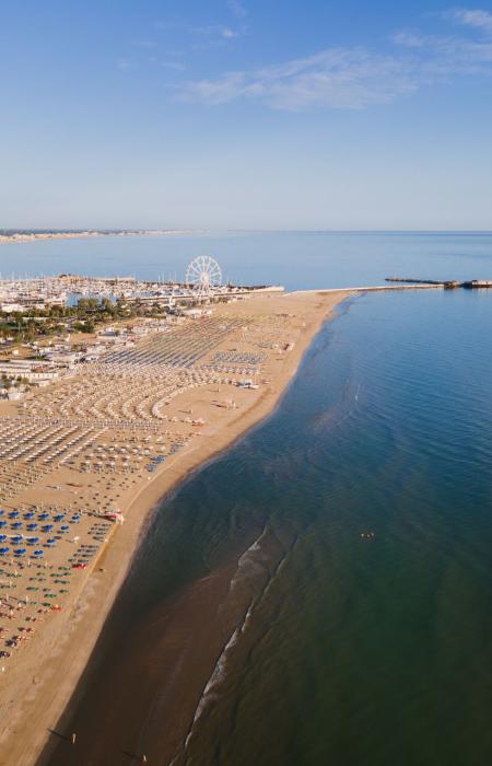 Spiaggia affollata con ombrelloni colorati e vista sulla ruota panoramica e il mare.