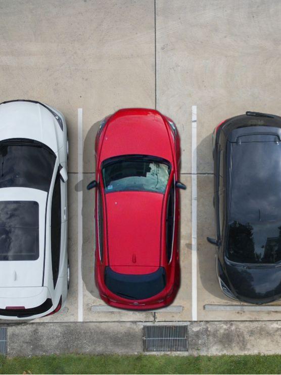 Vista dall'alto di tre auto parcheggiate: bianca, rossa e nera.