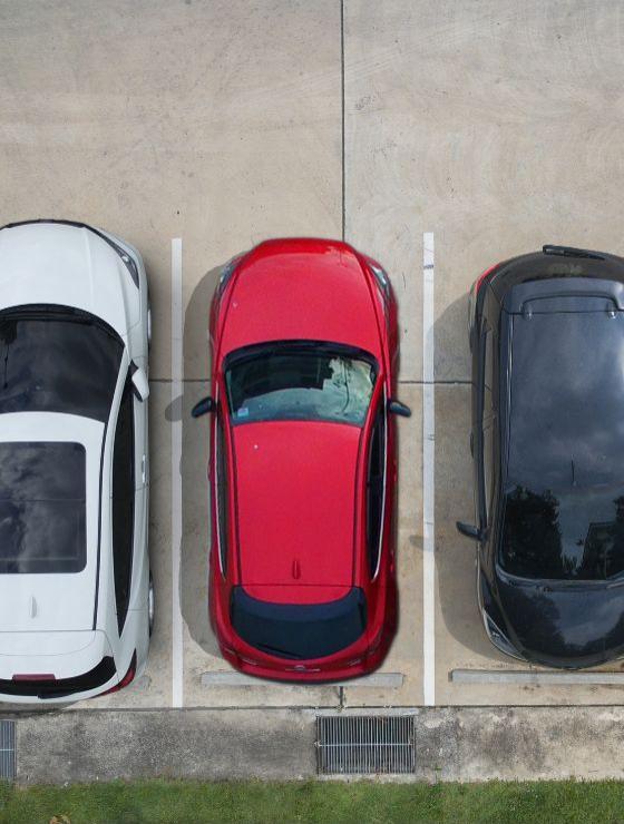 Tre auto parcheggiate in un parcheggio vuoto, viste dall'alto.