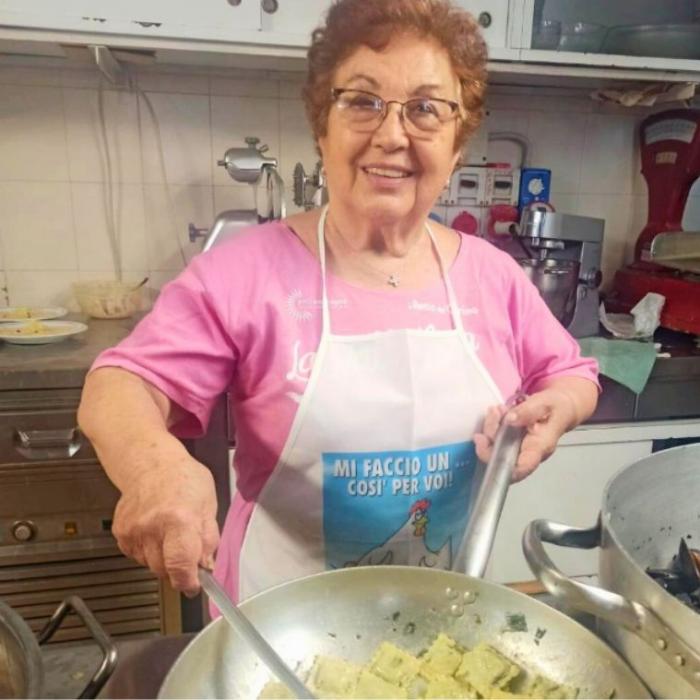 Signora cucina ravioli in una cucina professionale, indossa un grembiule divertente.