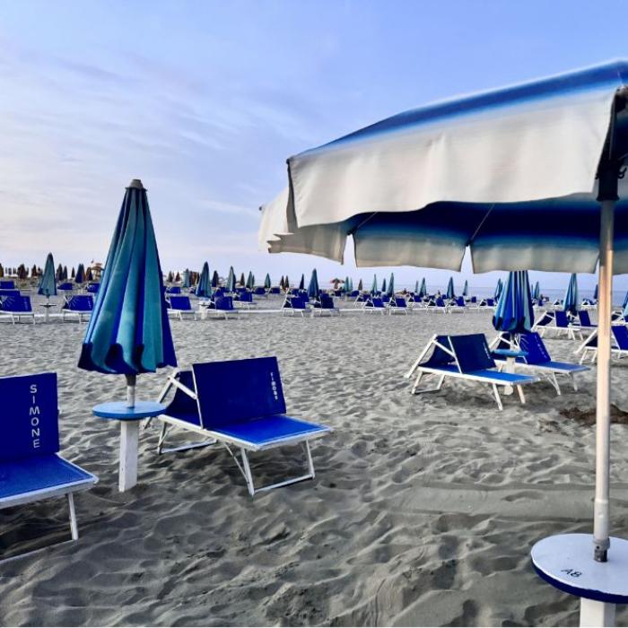 Spiaggia con ombrelloni e lettini blu, atmosfera tranquilla e cielo sereno.