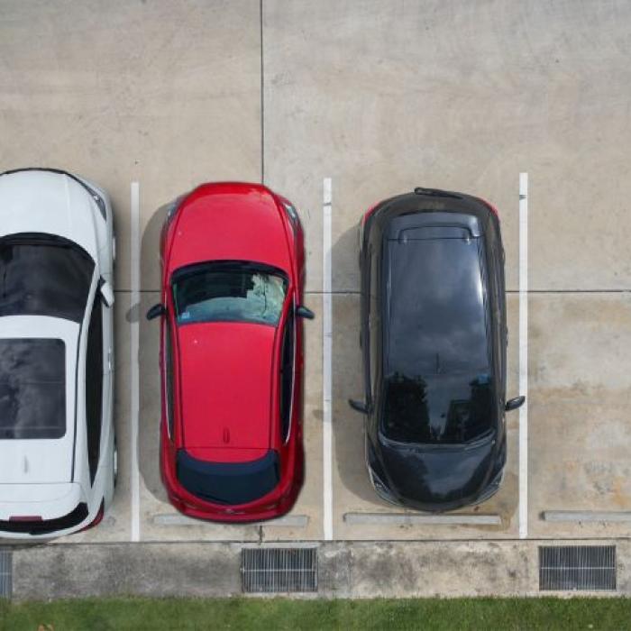 Tre auto parcheggiate in un parcheggio vuoto, viste dall'alto.