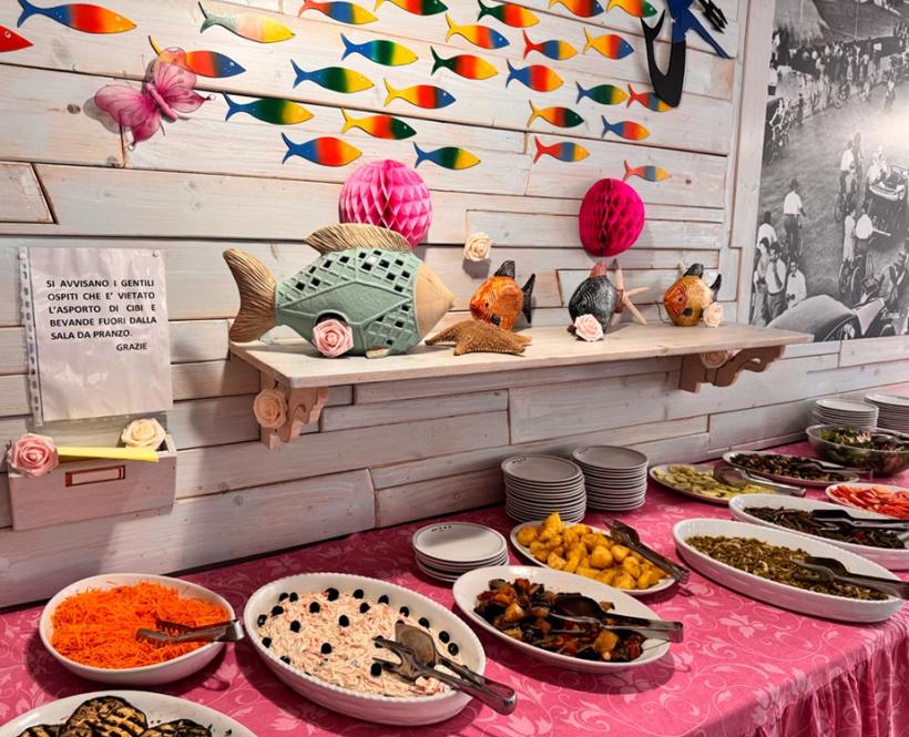 Buffet con piatti vari, decorazioni colorate e avviso di divieto di asporto.