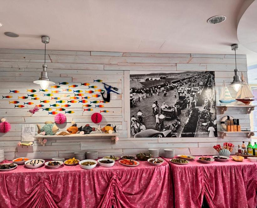 Buffet con tovaglia rosa, decorazioni marine e foto storica in bianco e nero.